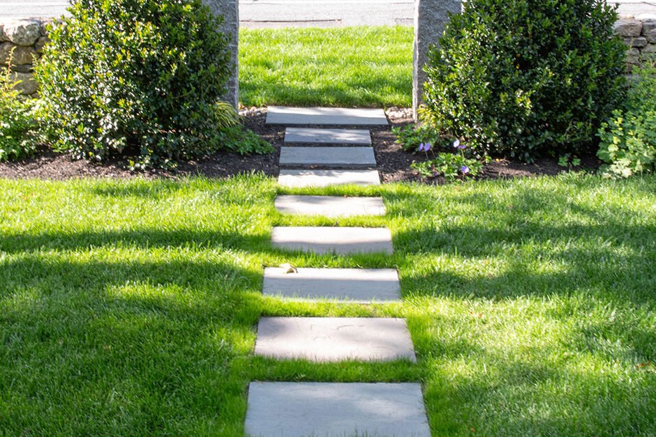 Stepping stone lawn path leads to granite posts, defining entry and movement with subtle structure and a refined residential feel.