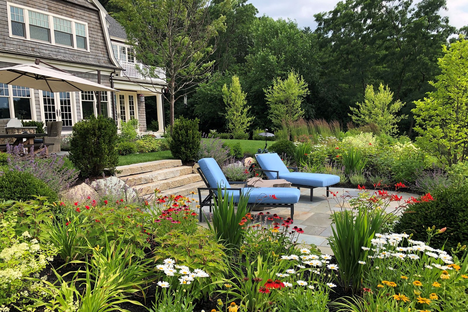 Bluestone lounge terrace surrounded by summer perennials creates seasonal charm and a serene space to sit, relax, and enjoy colorful garden views.