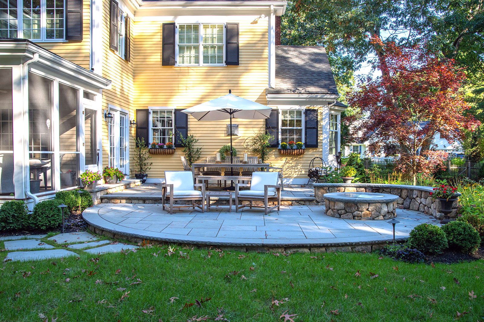 Curved bluestone terrace with central firepit fosters social gatherings and soft garden edges, creating fluid outdoor living in classic design.