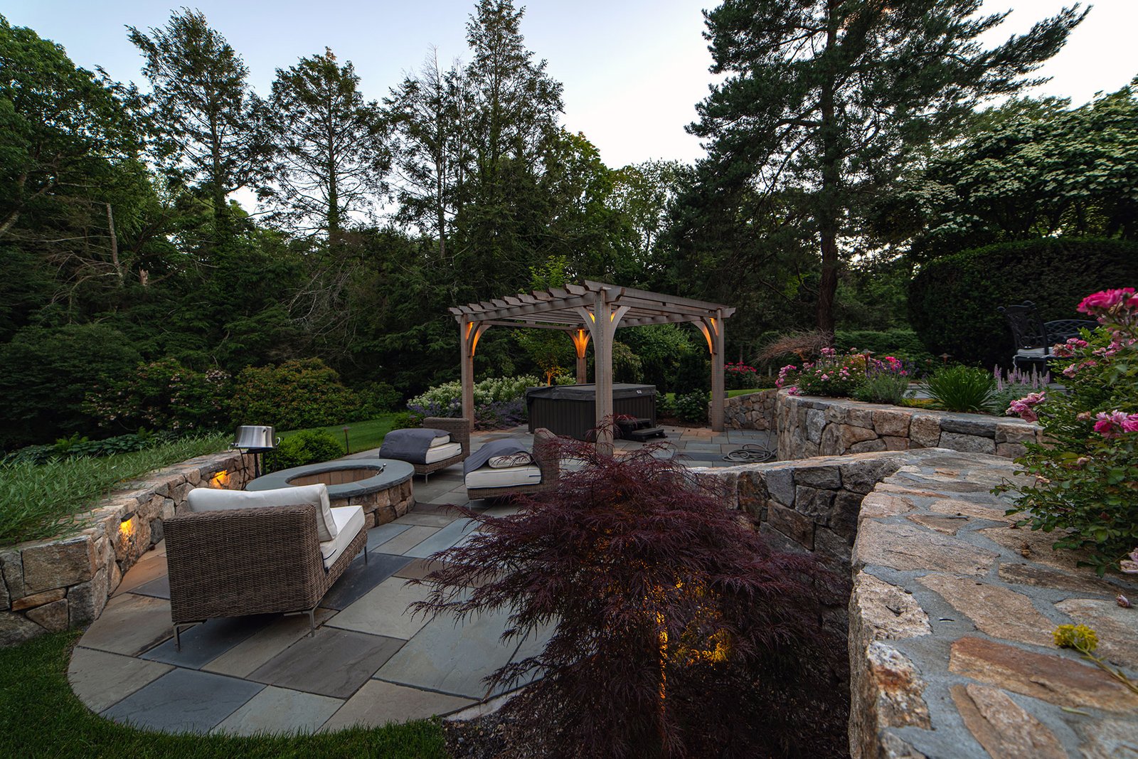 Natural stone terrace with pergola, firepit and lighting infuses this space with charm and soft nighttime ambiance for intimate dining and gatherings.