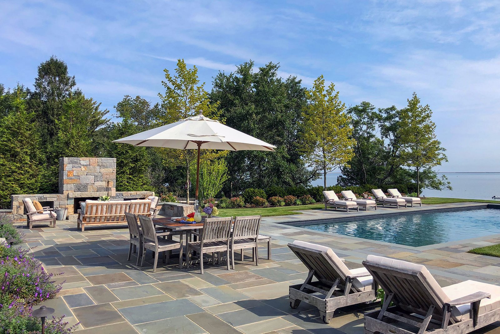 Duxbury, MA - Poolside bluestone patio with dining table and serene water views blends functional outdoor dining with scenic coastal atmosphere.