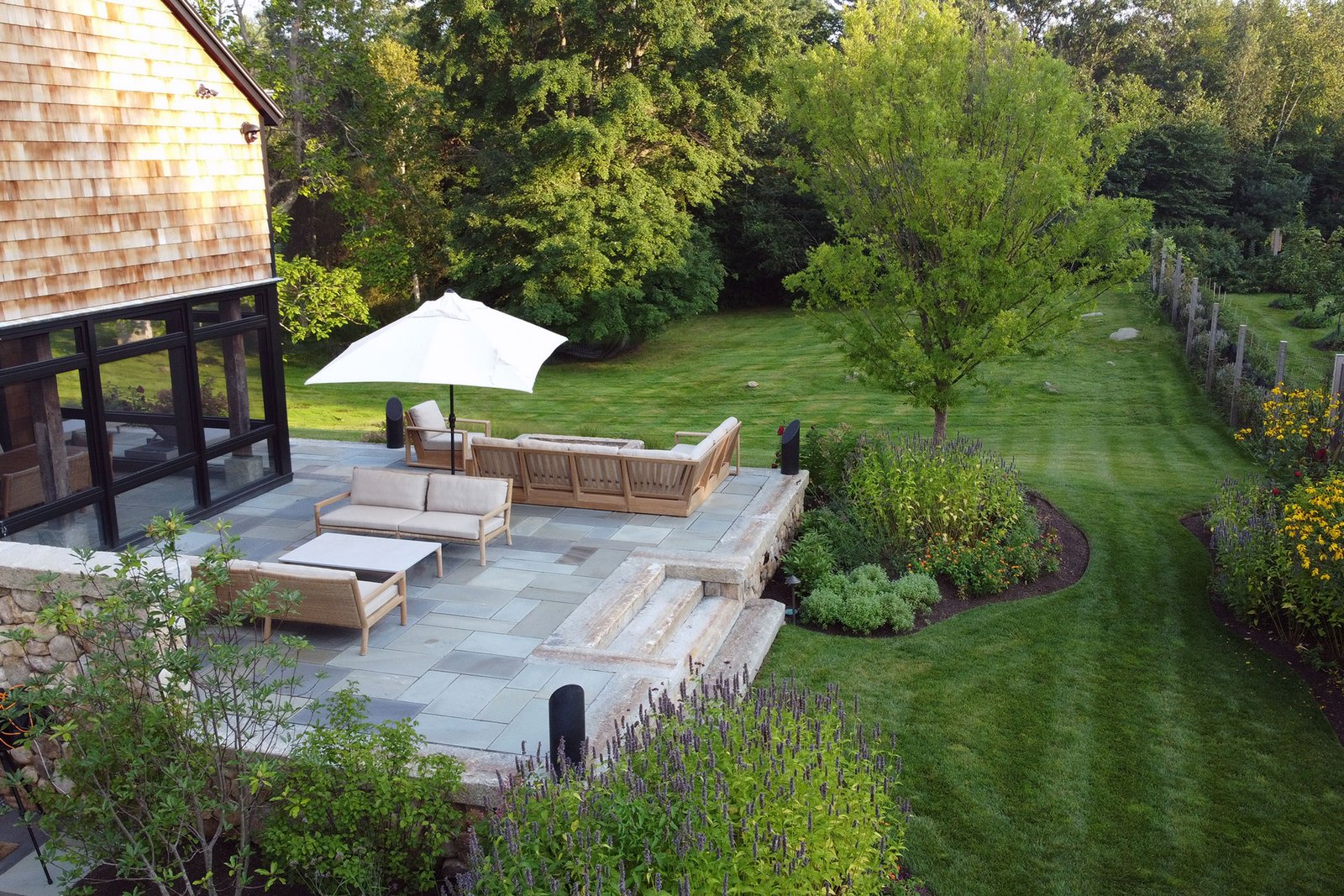 Carlisle, MA - Raised bluestone patio with garden borders and stone steps anchors this outdoor space with refined hardscape and soft perennial accents.