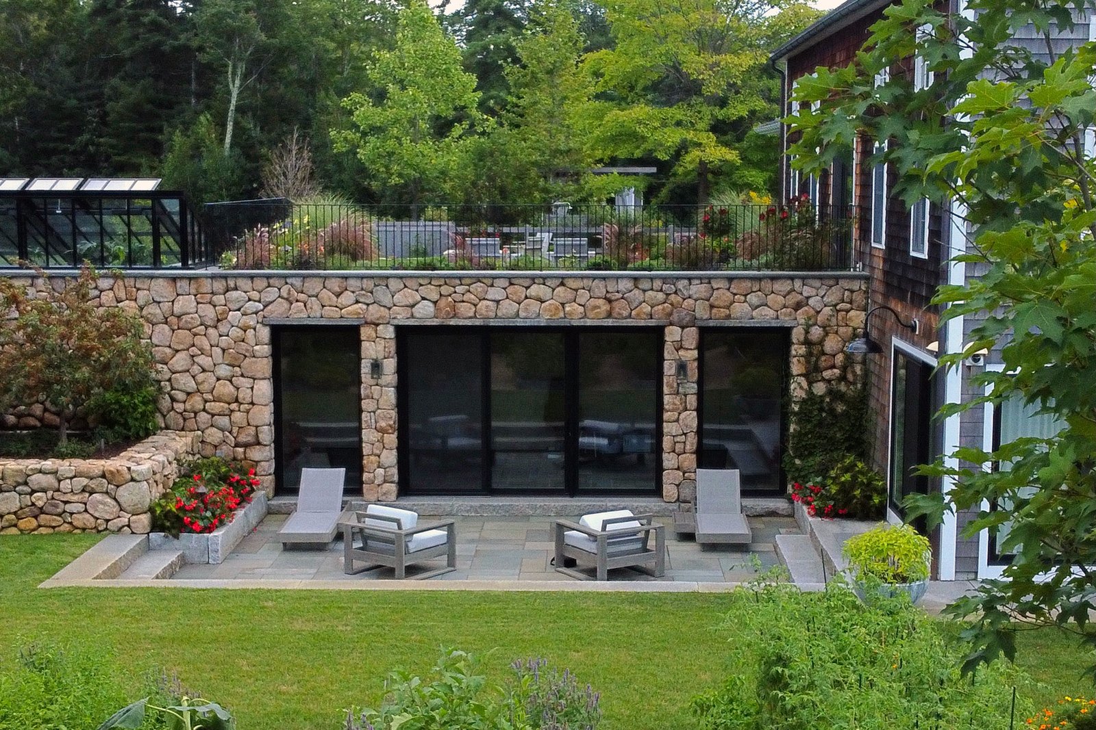 Carlisle, MA - Small seating terrace framed by fieldstone walls overlooks a manicured lawn, offering an intimate outdoor retreat with classical stone charm.