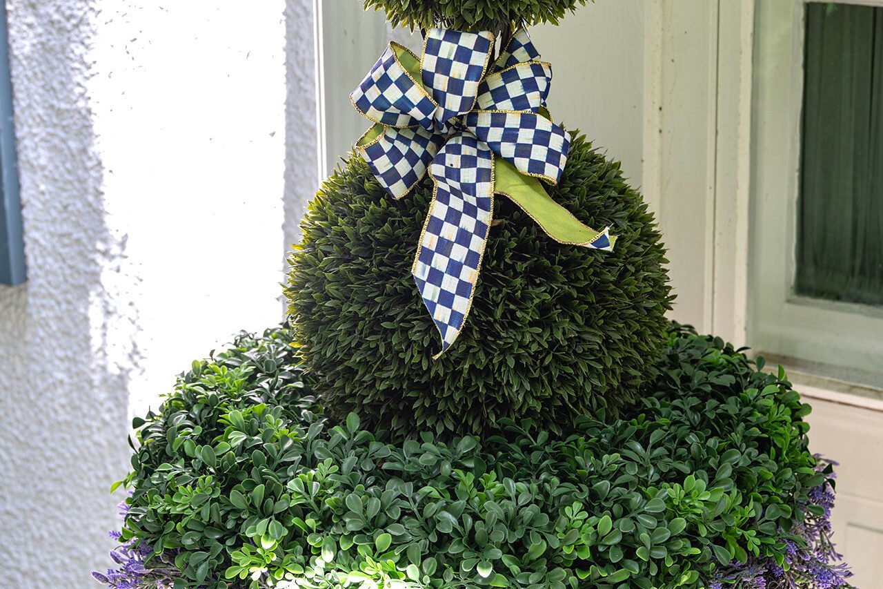 A classic urn supports a double ballwood topiary accented with ribbon, offering evergreen structure and minimal summer maintenance.