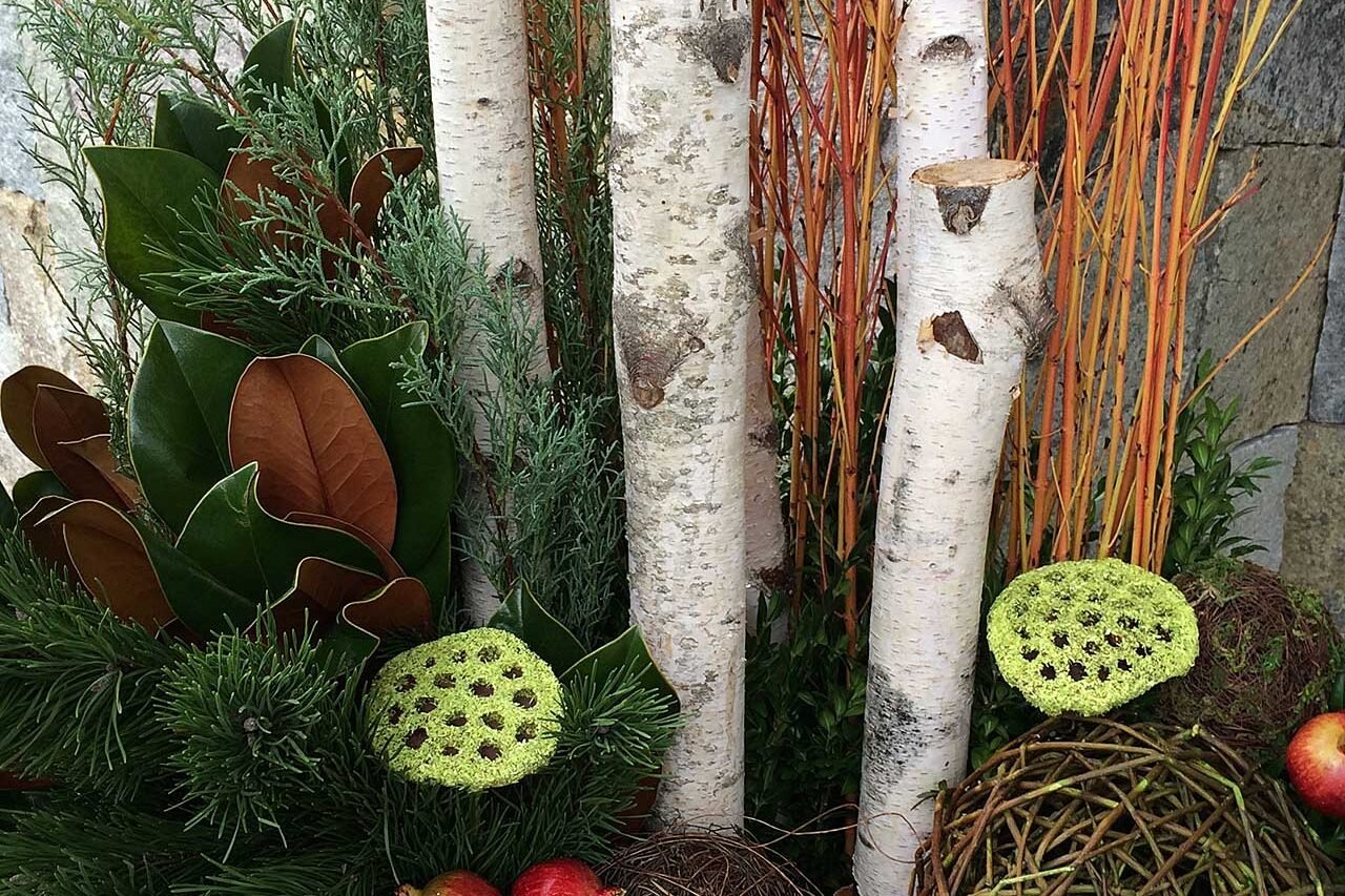 A winter urn arrangement combines evergreen branches, birch stems, and pinecones for texture and height, offering a durable seasonal accent that holds its form through cold weather.