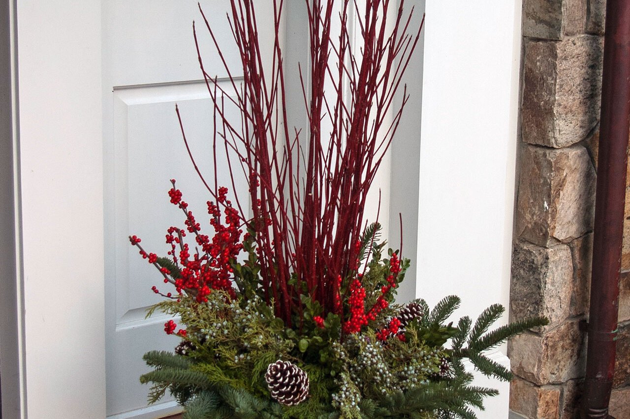 A substantial entry urn filled with evergreen boughs, red twig accents, and winter berries creates a welcoming seasonal display in Brookline, MA with strong curb appeal.