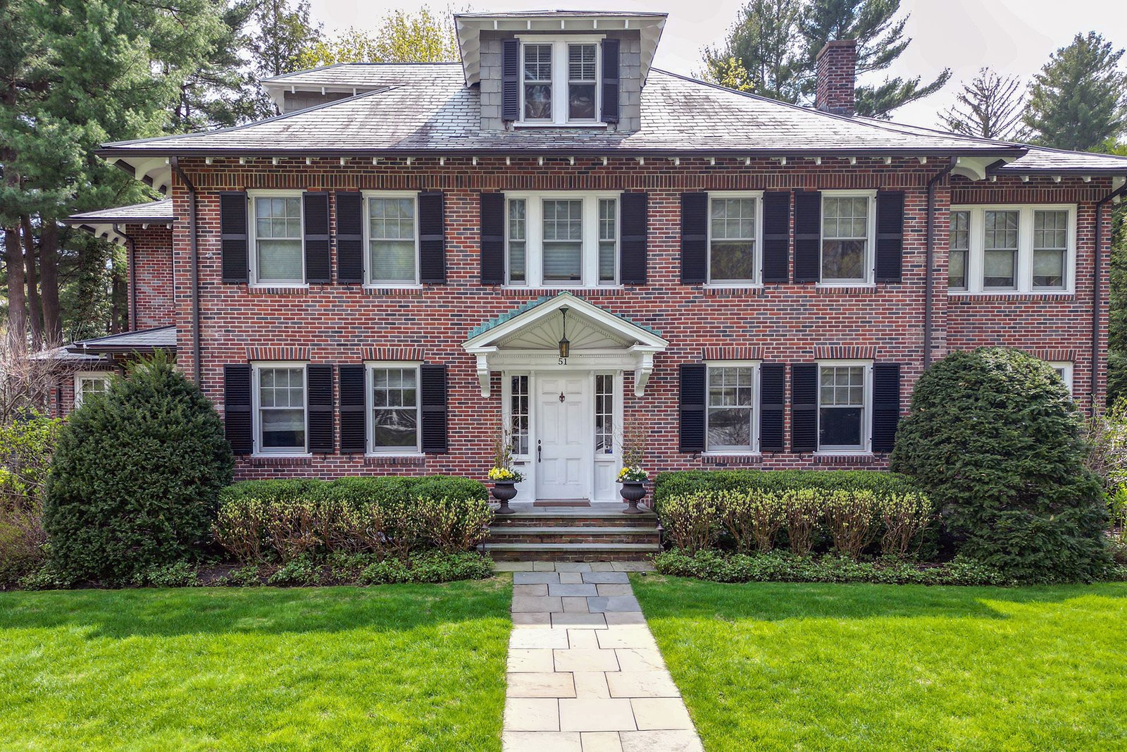 Formal boxwood hedges frame the front lawn of this brick colonial, reinforcing clean lines, symmetry, and year-round structure at the street edge.