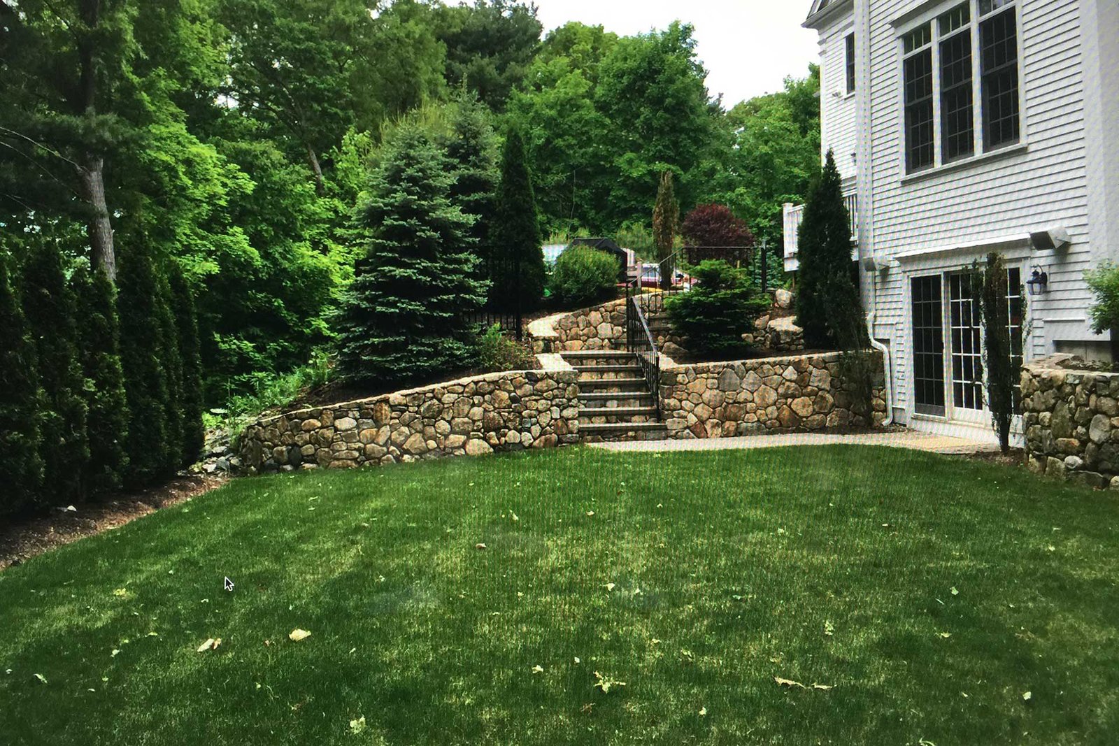 Backyard with retaining walls and lawn before patio renovation