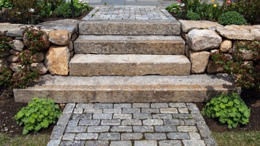 Granite steps descend to a cobblestone landing between fieldstone walls, with shrubs and hedges adding structure and refinement to this entry sequence in Weston.