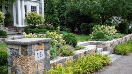 A low stone entry wall paired with granite steps establishes a clear arrival sequence, with adjacent hedges and foundation shrubs adding definition and a welcoming sense of enclosure.