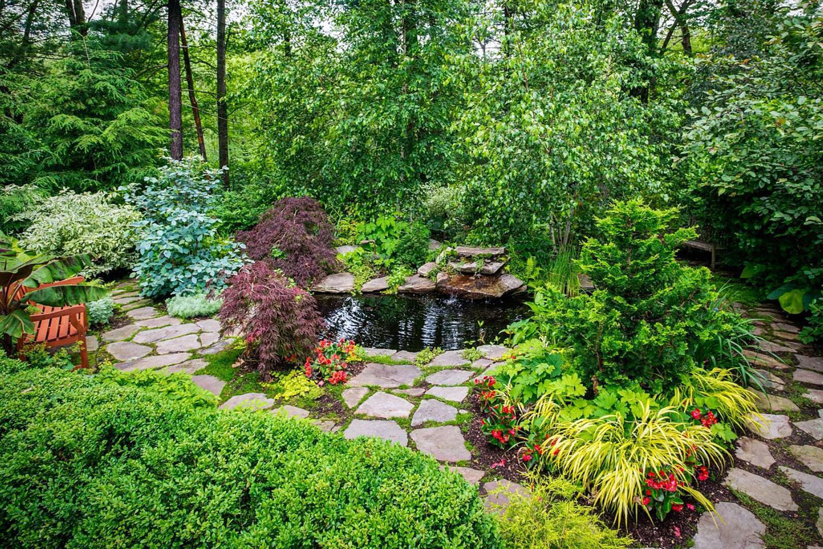 A natural woodland pond framed by stone paths and layered plantings adds movement, wildlife habitat, and a calming focal point to a Boston-area garden.