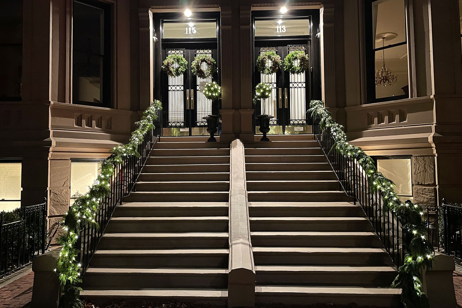 Boston brownstone front steps decorated with evergreen garland and warm holiday lighting.