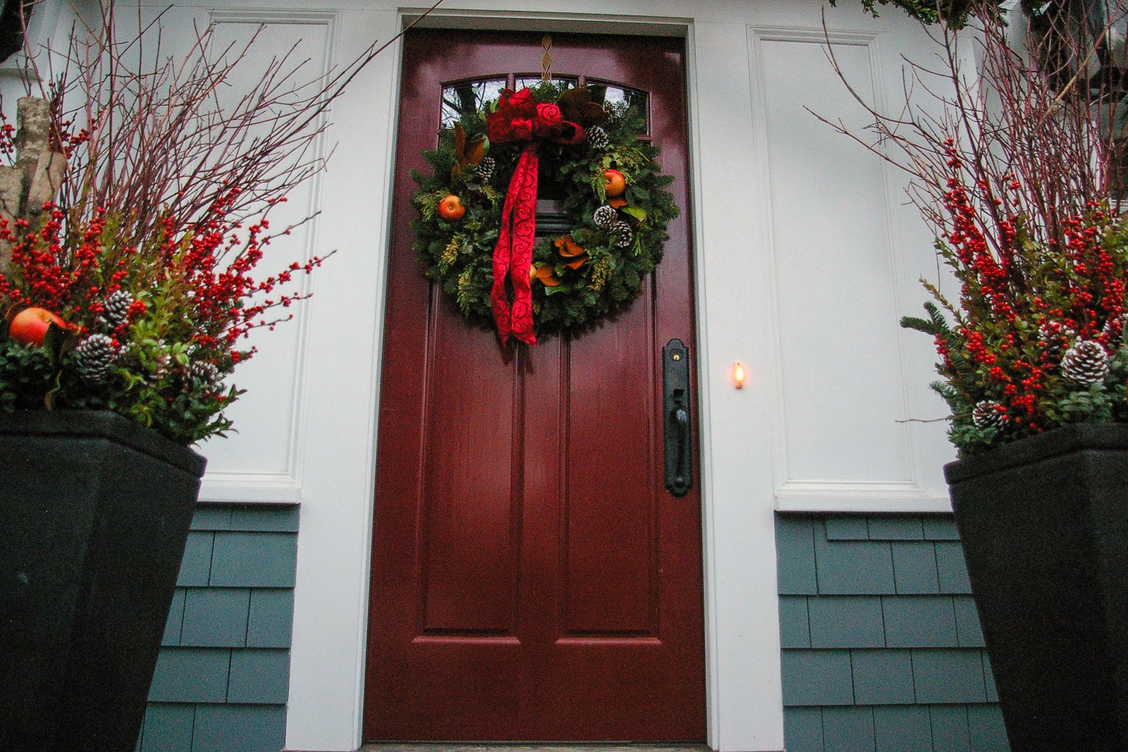 Front door decorated with an evergreen wreath and urn planters filled with seasonal greenery and red berries.