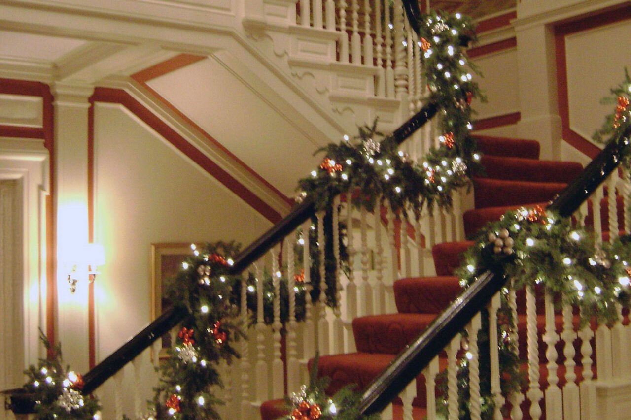 Historic Boston interior staircase decorated with evergreen garland, warm white lights, and red holiday accents.