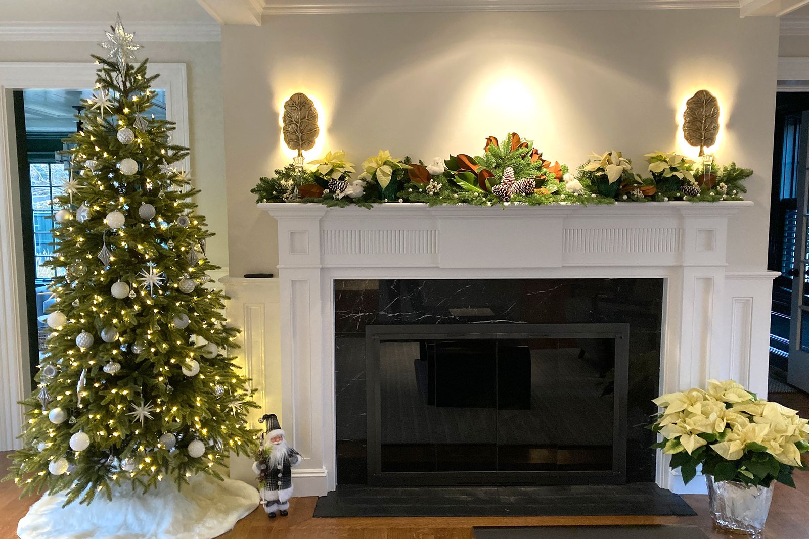 An elegant interior holiday scene pairs a softly decorated Christmas tree with a fireplace mantel accented in white seasonal décor, creating a calm and refined winter atmosphere.