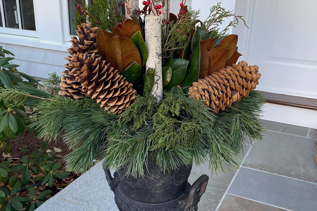 A cast-iron urn on a Needham porch is filled with birch branches, pinecones, and fresh evergreens for a classic, understated winter display.