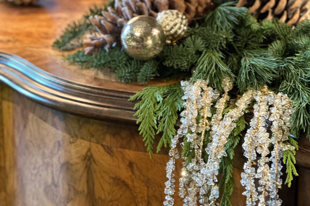 A richly layered winter mantel in Newton features pinecone garland, crystal accents, and seasonal greenery, creating an elegant focal point around the fireplace.