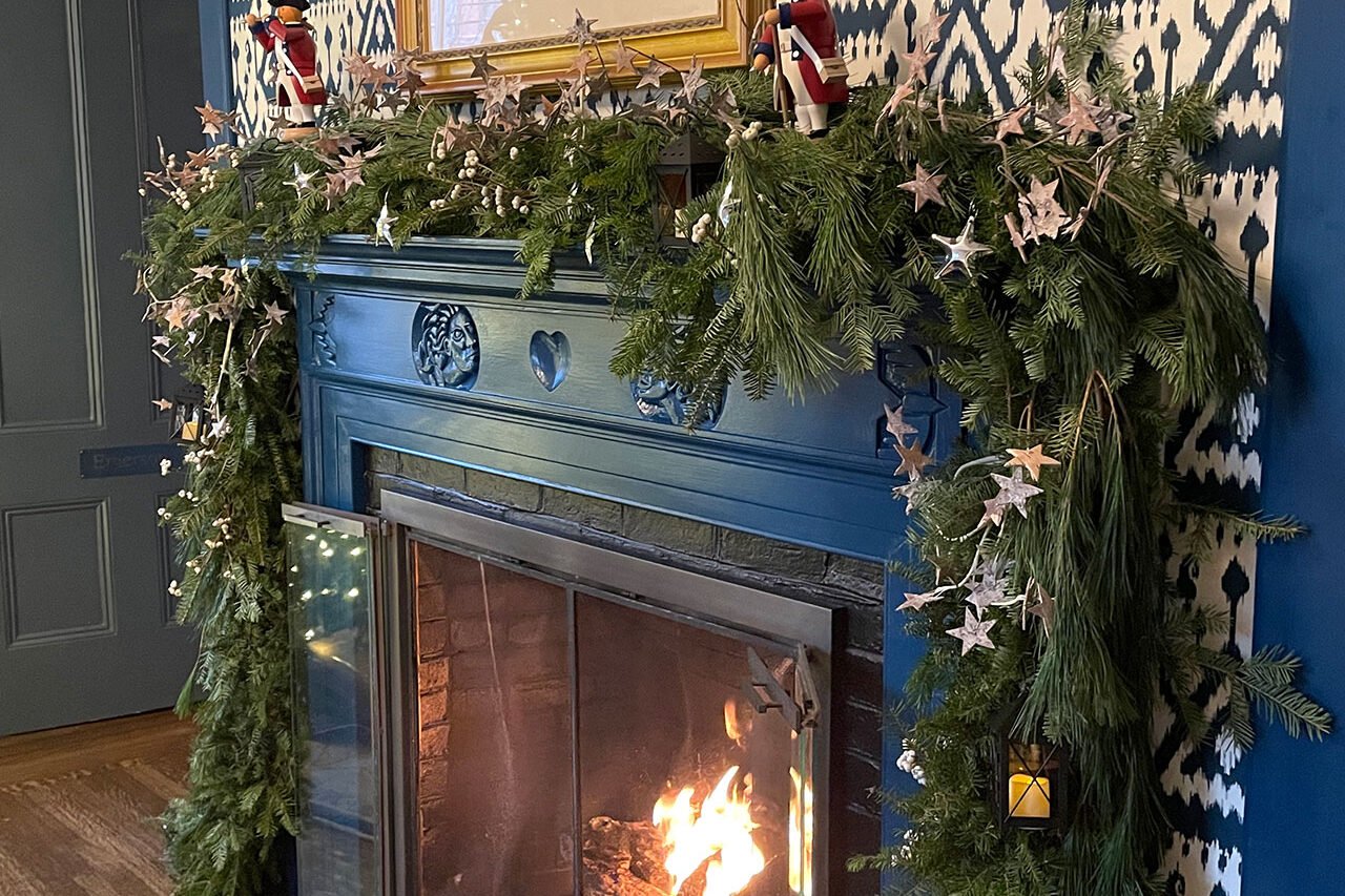 A fireplace mantel dressed with evergreen garland and star accents, creating a warm, seasonal focal point indoors.